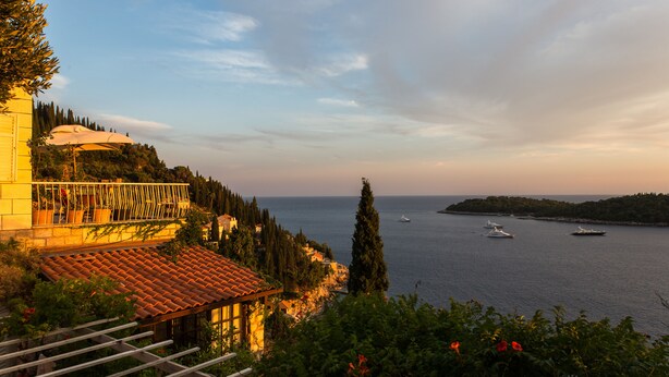 Una villa costera con terraza con vistas al mar, con techo de tejas y abundante vegetación.