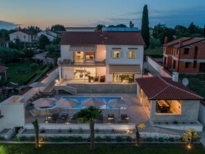 Une grande maison avec une piscine, un espace extérieur aménagé pour s’asseoir et une terrasse bien éclairée.