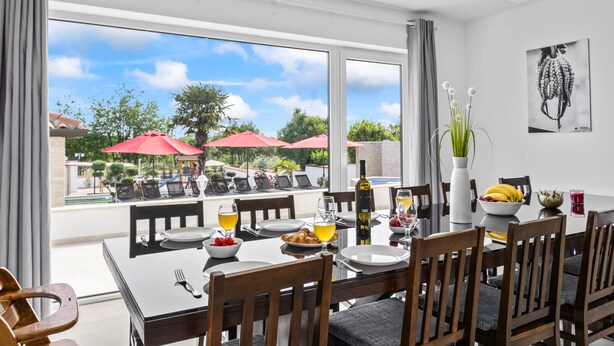 A dining area with a view of the outdoors, featuring a table set for four, chairs, and a vase with flowers. - Villa Anela with pool in Porec, Istria (Buici)