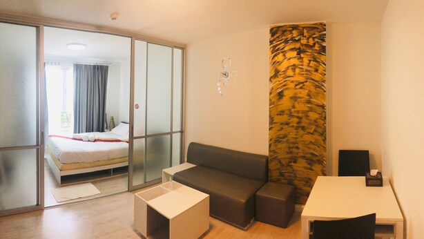 A modern hotel room with a bed, a sofa, a small table, and a decorative wall panel. - D condo Hyde Chiangrai. Authentic Thai hospitality. Room service is provided. (phan)