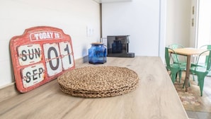 Een kamer met een houten vloer, een geweven vloerkleed, een rood bord waarop staat 'TODAY IS SUN 01 SEP', een blauwe vaas en groene stoelen.