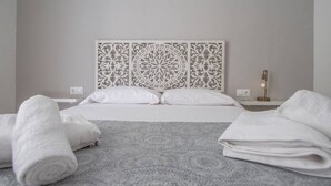 Een netjes opgemaakt bed met witte lakens, een tapijt met een grijs patroon en een decoratief hoofdeinde.
