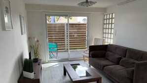 Ein Wohnzimmer mit einem braunen Sofa, einem Holztisch, einem grünen Sessel und einer Glastür, die zu einem Außenbereich mit Holzzaun führt.