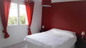 Ein Schlafzimmer mit einem großen Bett, roten Vorhängen, einer weißen Decke und einem Fenster mit Blick auf Grünflächen.