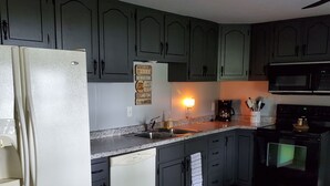 A kitchen with dark green cabinets, a white refrigerator, a microwave, and a sink.