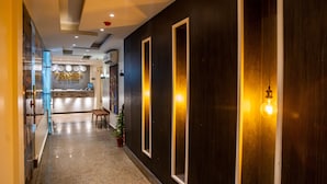 Un pasillo de hotel con una zona de recepción, un mostrador de recepción, un banco y una planta en maceta.