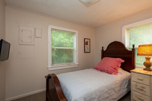 A bedroom with a single bed, a nightstand, a lamp, a window with blinds, and a wall-mounted TV. - Fairhope 3BR house. 4min to Grand Hotel, 7min to Dwntown Fhope, 44min to Gulf (Fairhope)