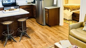 A compact kitchen with a refrigerator, stove, and bar stools. - Kuby's Place, Downtown Shiner Casita (Shiner)