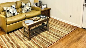 A living room with a brown leather sofa, a wooden coffee table, and a patterned rug. - Kuby's Place, Downtown Shiner Casita (Shiner)