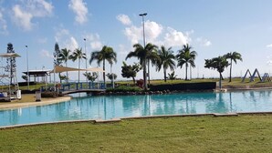 Una piscina con un puente, palmeras y un área con césped.