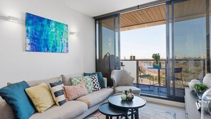Un salon moderne avec un canapé, une table basse et une grande fenêtre donnant sur un paysage urbain.