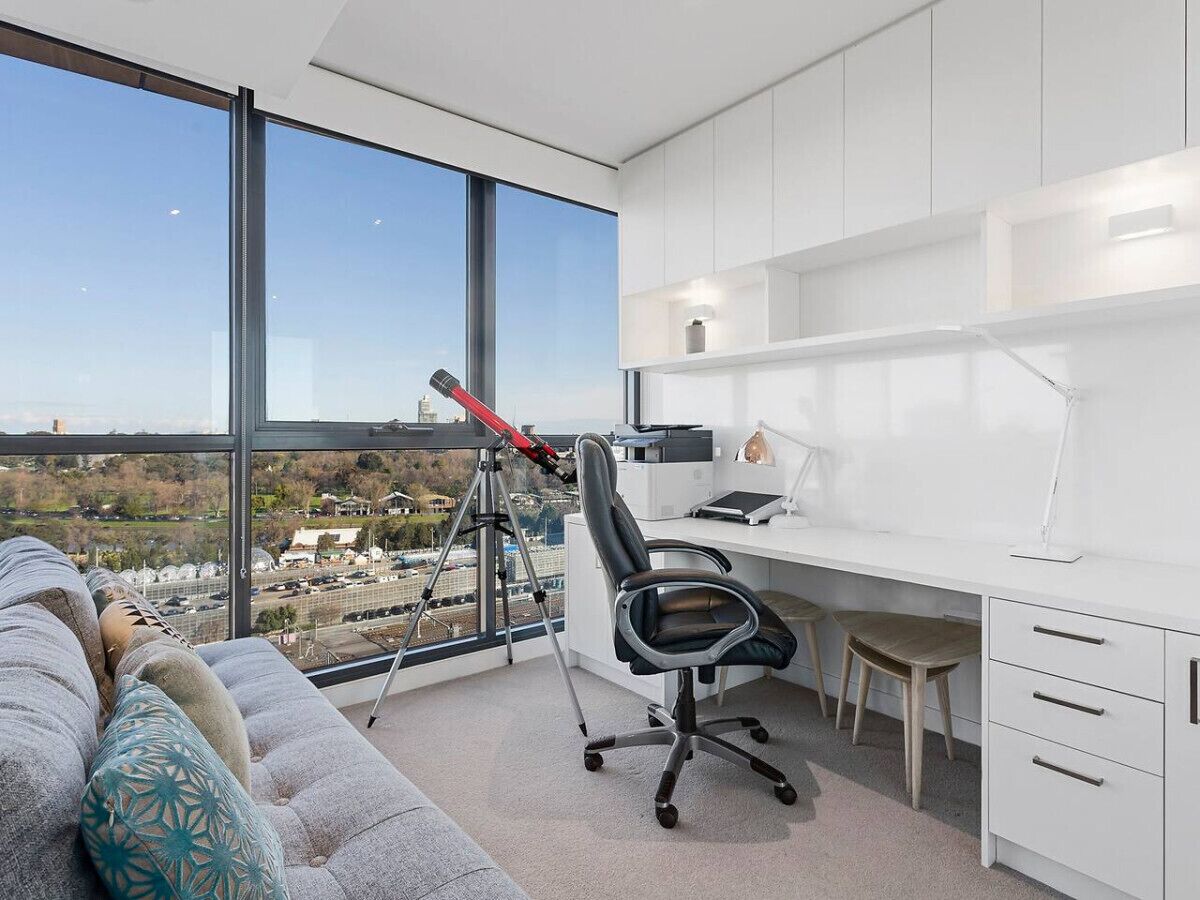 A modern office with a large desk, a comfortable sofa, and a telescope.