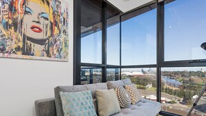 Un salon moderne avec un canapé gris, des coussins à motifs et une grande fenêtre donnant sur la ville.