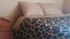 Uma cama com colcha estampada, uma mesa de cabeceira de madeira e um painel de parede colorido.
