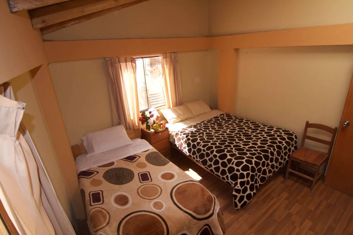 Ein kleines Schlafzimmer mit zwei Betten, einem Nachttisch, einem Stuhl und einem Fenster mit Vorhängen.