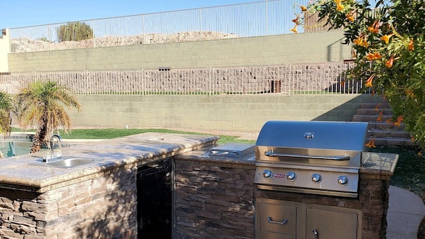 Une cuisine extérieure dotée d’un plan de travail en pierre, d’un barbecue et d’un évier.
