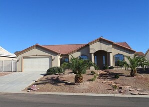 A two-story house with a garage, a driveway, and a landscaped front yard with palm trees and shrubs.