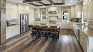 A spacious kitchen with wooden flooring, stainless steel appliances, and a central island with bar stools.