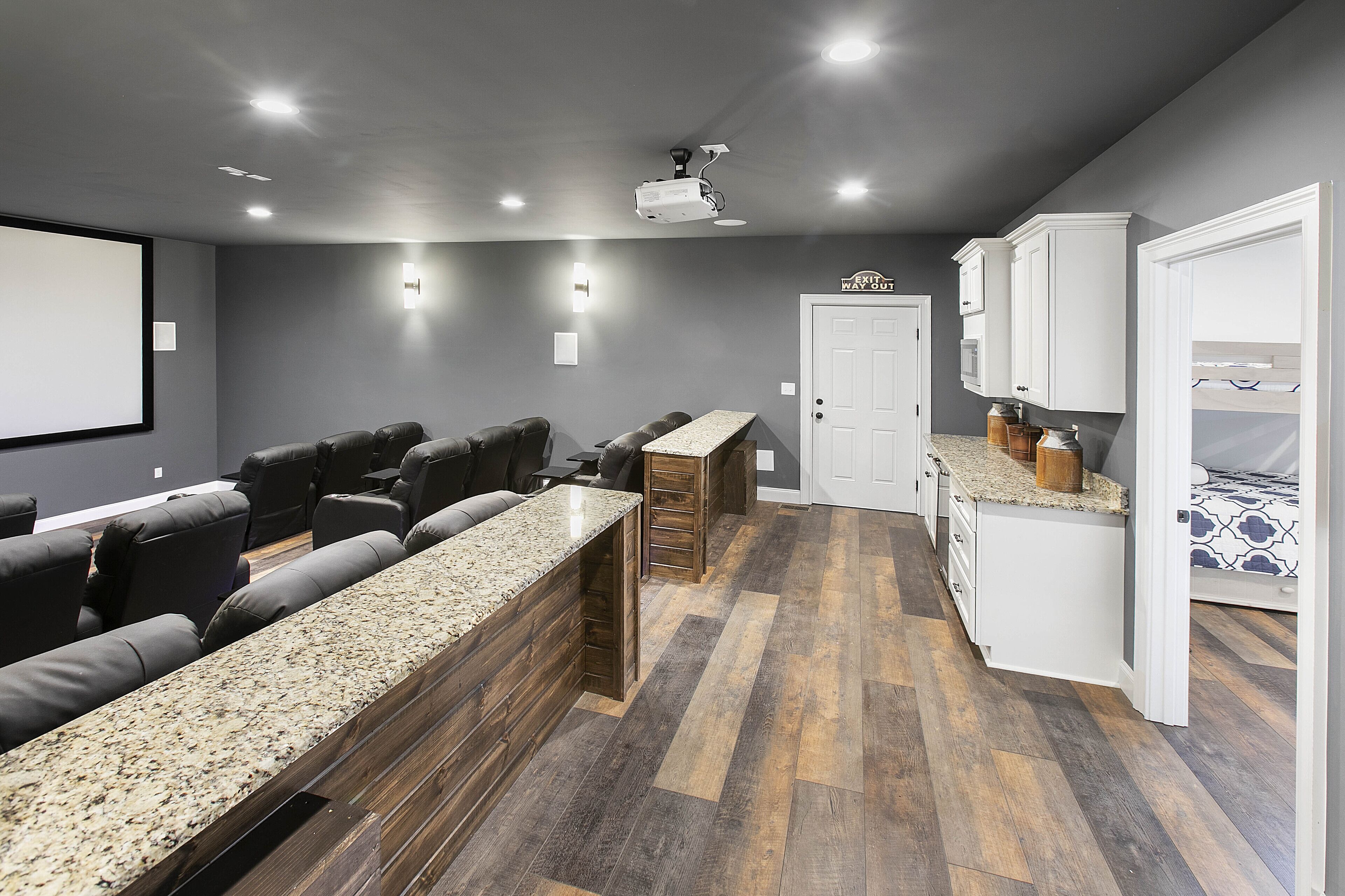 A home theater with a large screen, comfortable seating, and a kitchen area with cabinets and a countertop.