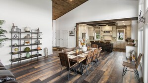 A spacious dining area with a wooden table and chairs, a dark wood floor, and a kitchen in the background.