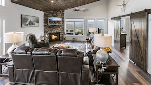 A spacious living room with a fireplace, leather recliner, and a large window offering a view of the mountains.