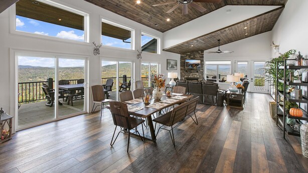 A spacious living area with a large dining table, multiple chairs, a kitchen area, and a balcony with a scenic view.
