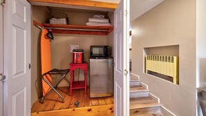 A compact kitchen with a refrigerator, microwave, and a red stool.