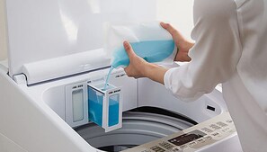 A person pouring a blue liquid into a washing machine.