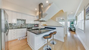 A modern kitchen with white cabinets, a stainless steel range hood, and a black countertop island with bar stools.