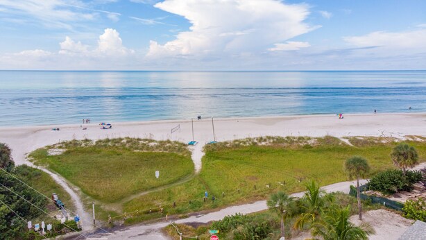 A beach with a clear view of the ocean, a sandy path leading to the beach, and some greenery in the foreground.