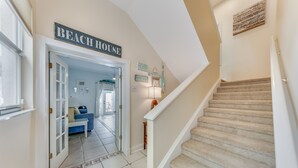 A hallway leading to a room labeled "BEACH HOUSE" with a carpeted staircase and a view of the living area.