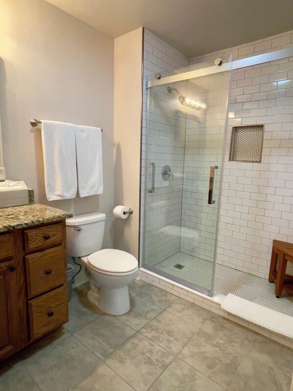 Une salle de bain comprenant des toilettes, une douche fermée par des parois en verre et un meuble-lavabo en bois doté de tiroirs.