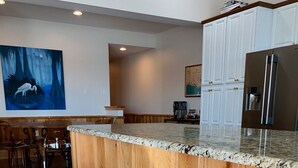 Une cuisine moderne avec des meubles en bois, un plan de travail en granit et deux tabourets de bar.