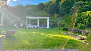 A garden with a white pergola, outdoor furniture, and a stone wall.
