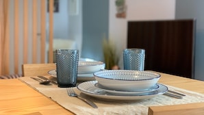 A dining table set with blue and white patterned plates, two textured glassware, and cutlery on a beige placemat. - Modern and romantic house with large garden to relax (Ponta Delgada)