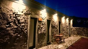 A stone building with three illuminated doors and a small outdoor seating area with a table and chairs. - Modern and romantic house with large garden to relax (Ponta Delgada)