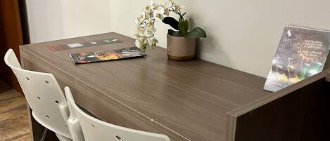 Una mesa de madera con dos sillas blancas, una orquídea en maceta y una revista sobre la mesa.