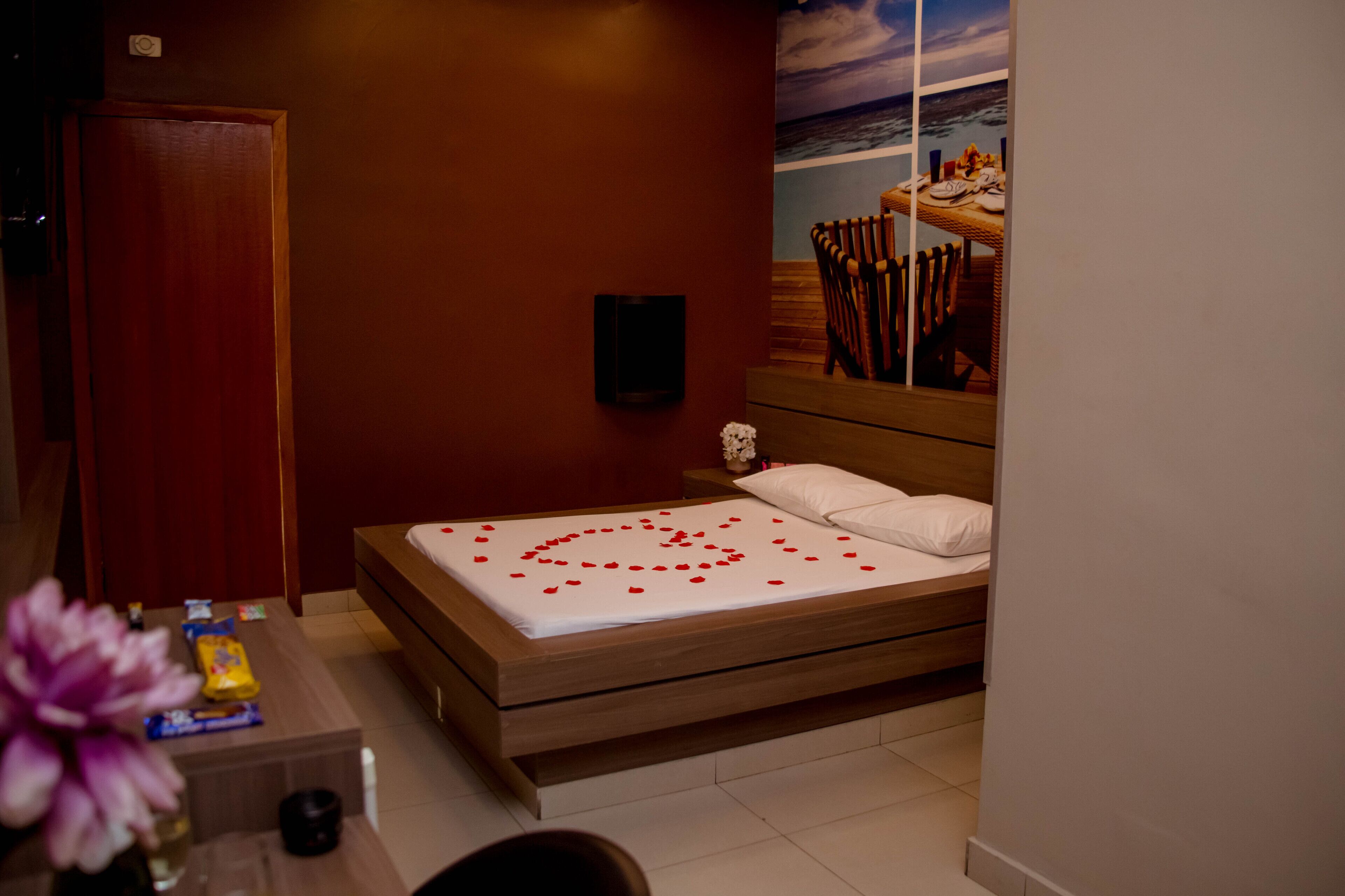 Un dormitorio con una cama de madera, una mesita de noche, un televisor montado en la pared y un cuadro con una escena de playa.