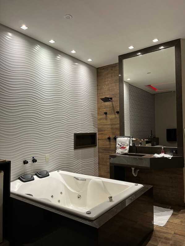 A modern bathroom with a large freestanding bathtub, a vanity with a mirror, and a textured wall design. - Motel Stilo (Contagem)