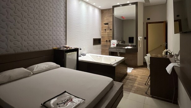 Una habitación de hotel moderna con una cama grande, un baño con bañera y un comedor.