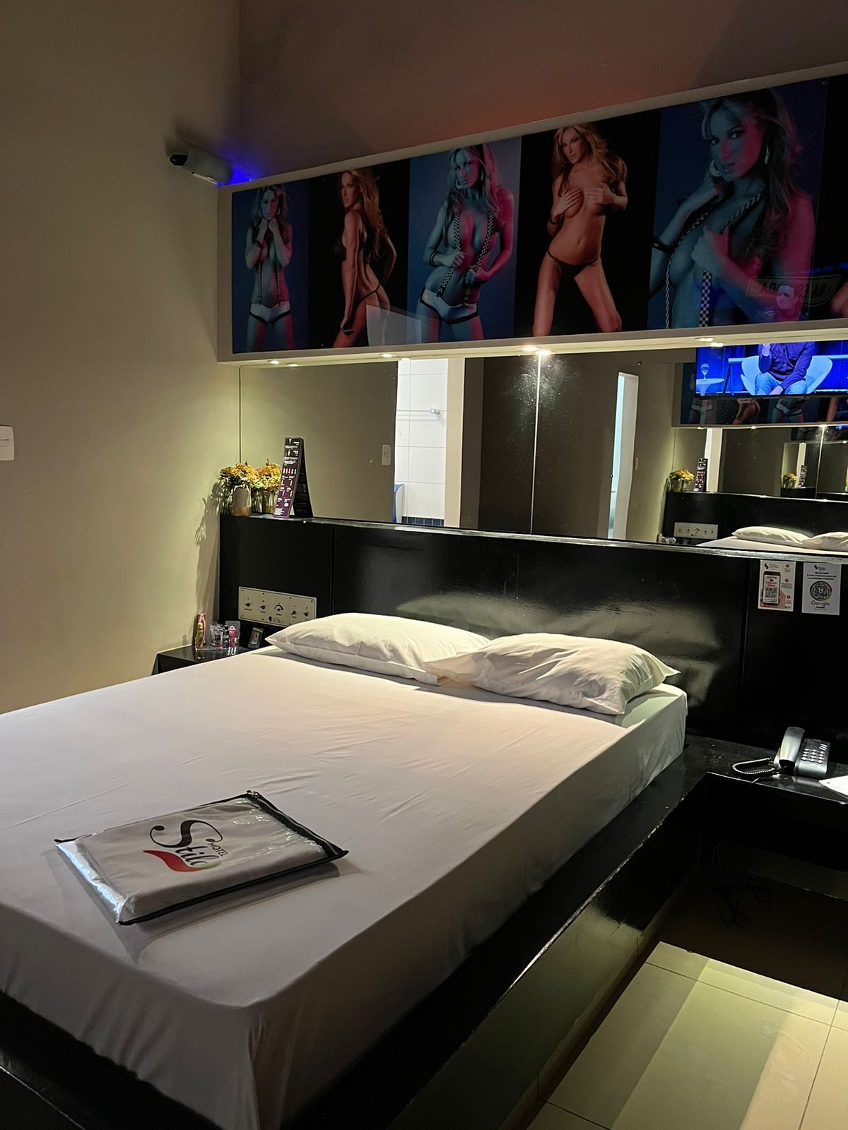 A hotel room with a large bed, a bedside table with a lamp, a mirror, and a TV mounted on the wall.