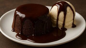 Un piatto dessert con un tortino dal cuore fondente al cioccolato e una pallina di gelato alla vaniglia irrorata di salsa al cioccolato.
