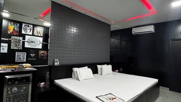 Un dormitorio moderno con una cama grande, un minibar y una pared decorada con obras enmarcadas.