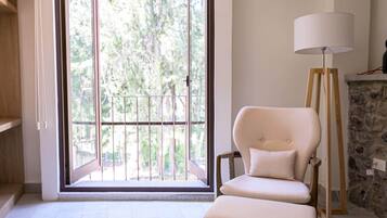 Een kamer met een schuifdeur naar een balkon, een witte fauteuil, een vloerlamp en een stenen haard.