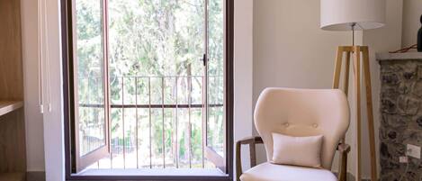 A room with a sliding glass door leading to a balcony, a white cushioned chair, a floor lamp, and a stone fireplace.
