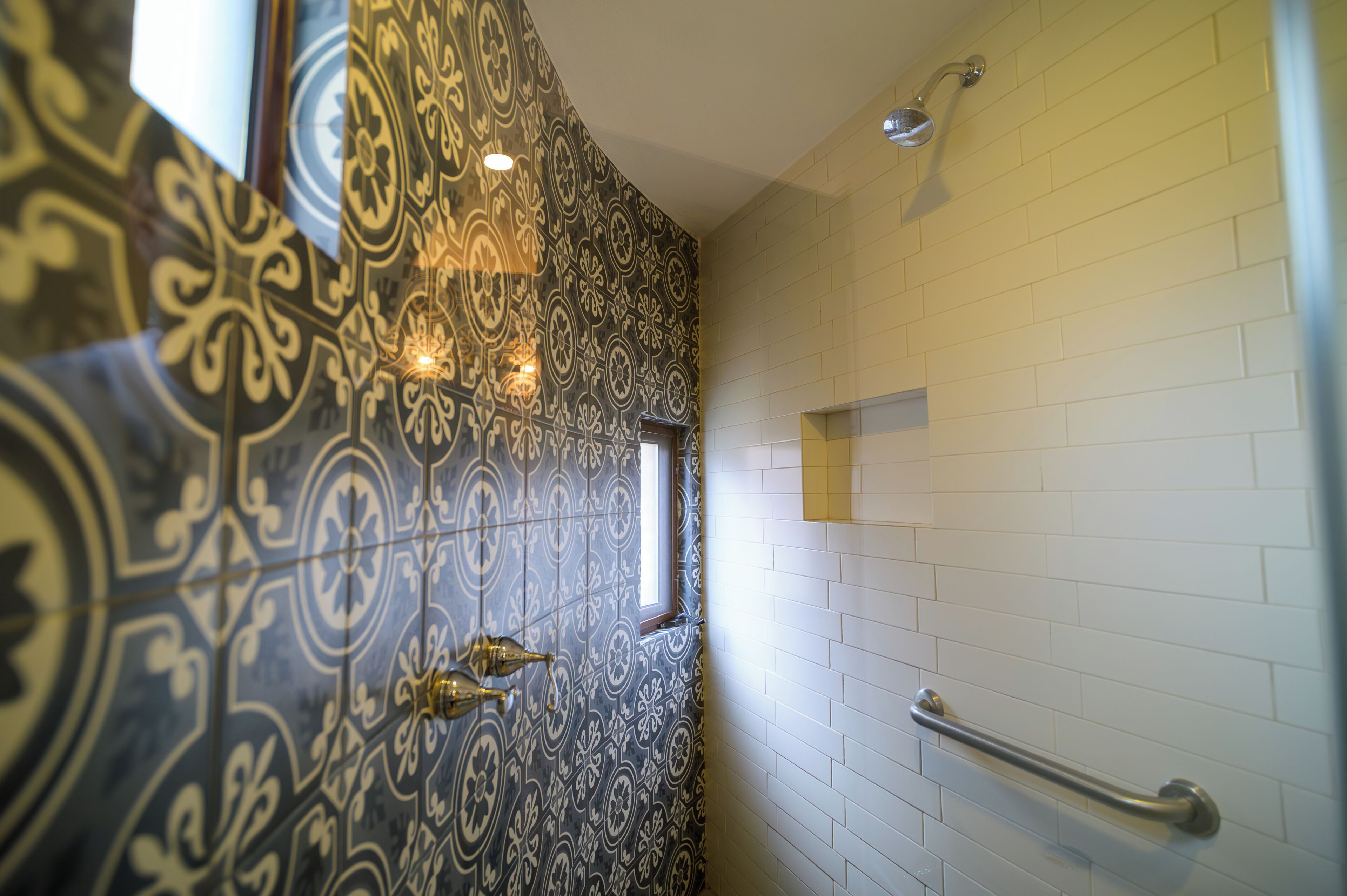 A bathroom with patterned tiles, a window, a showerhead, and a handrail.
