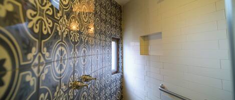 A bathroom with patterned tiles, a window, a showerhead, and a handrail.