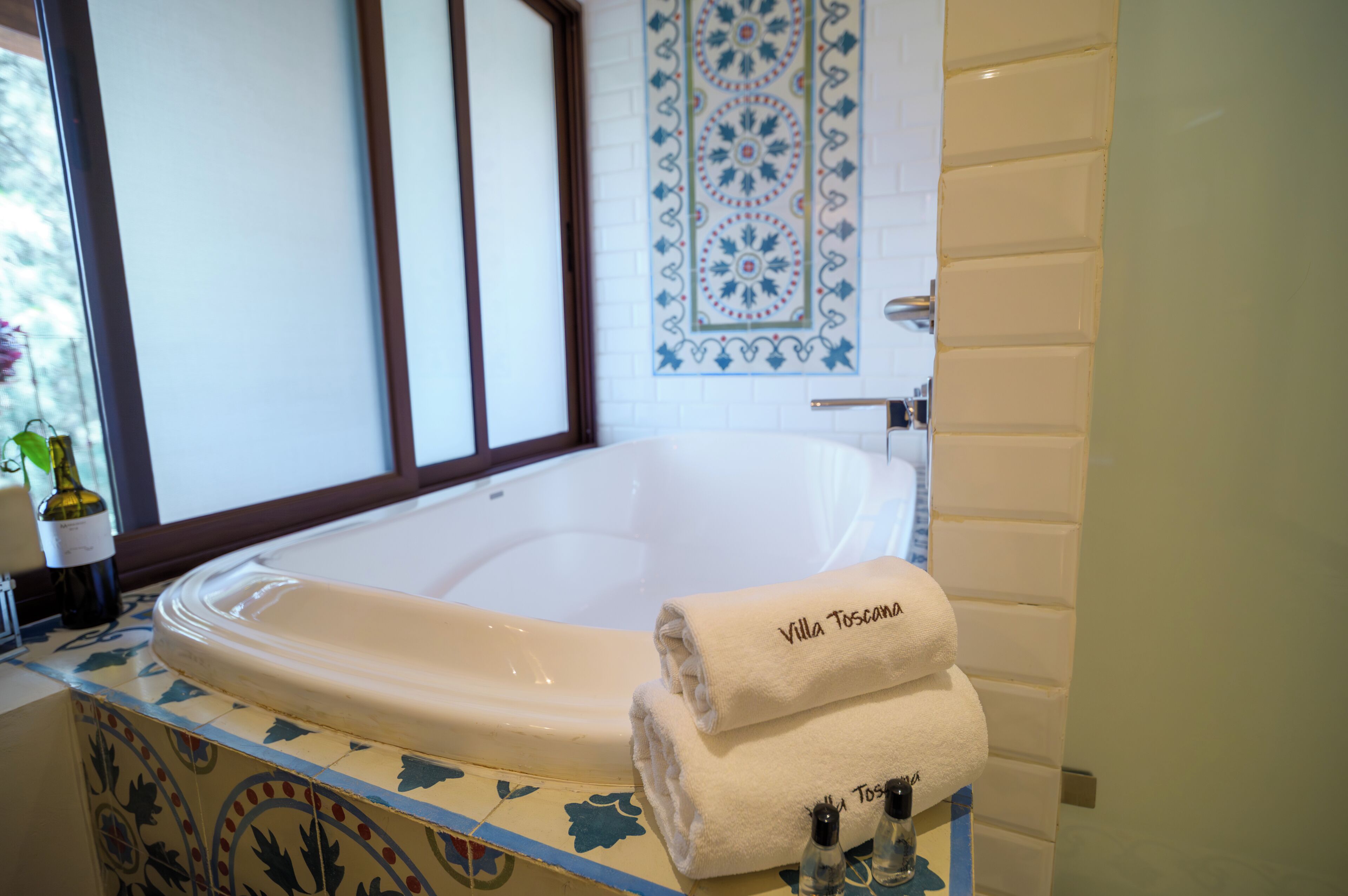 Un baño con una bañera grande, una pared decorada con azulejos y una toalla que dice "Villa Toscana".