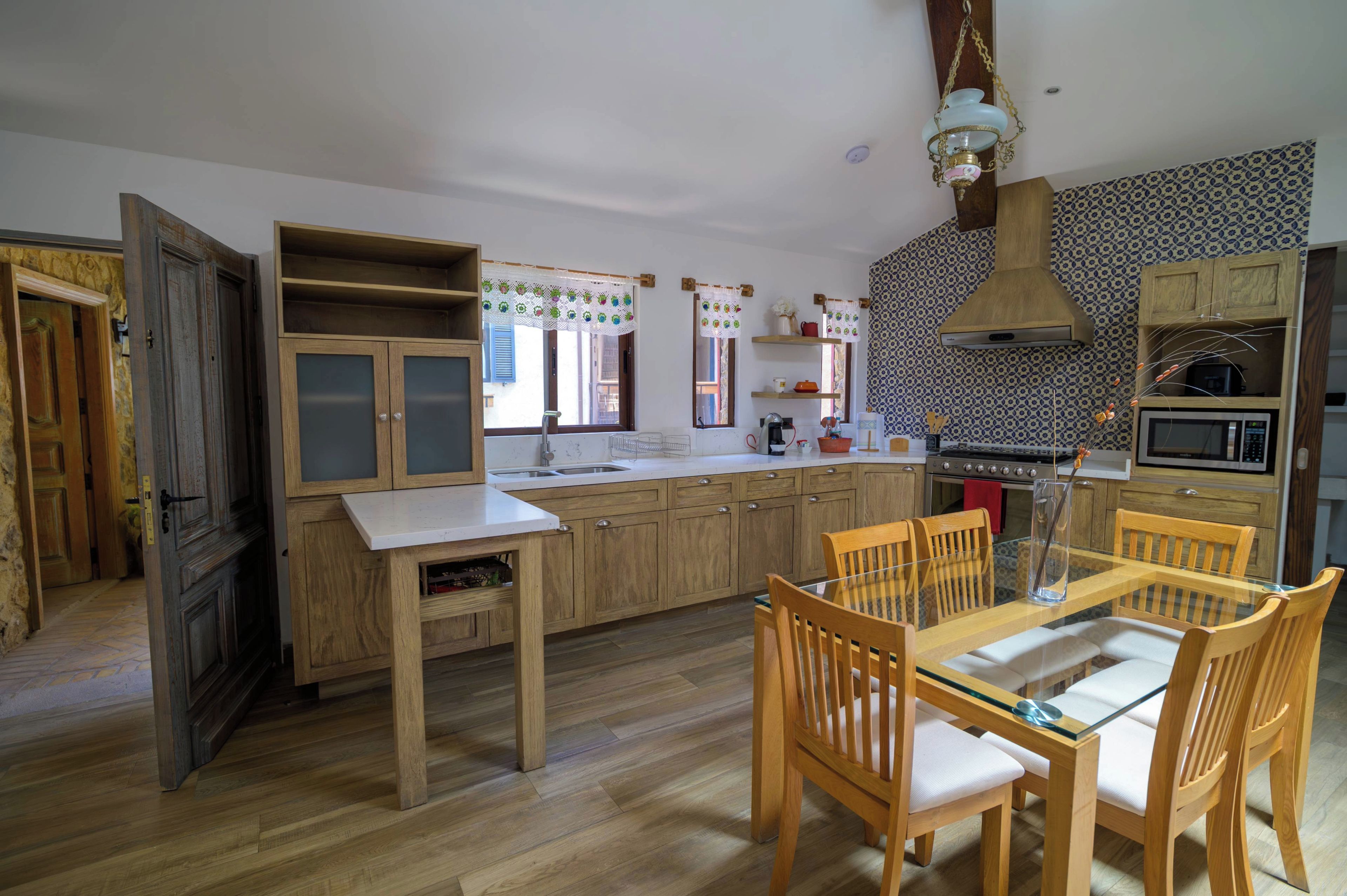 Una cocina con armarios de madera, una mesa de comedor con sillas, una lámpara colgante y un salpicadero decorado.