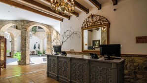 A lobby with stone arches, a reception desk, a chandelier, and a large mirror.